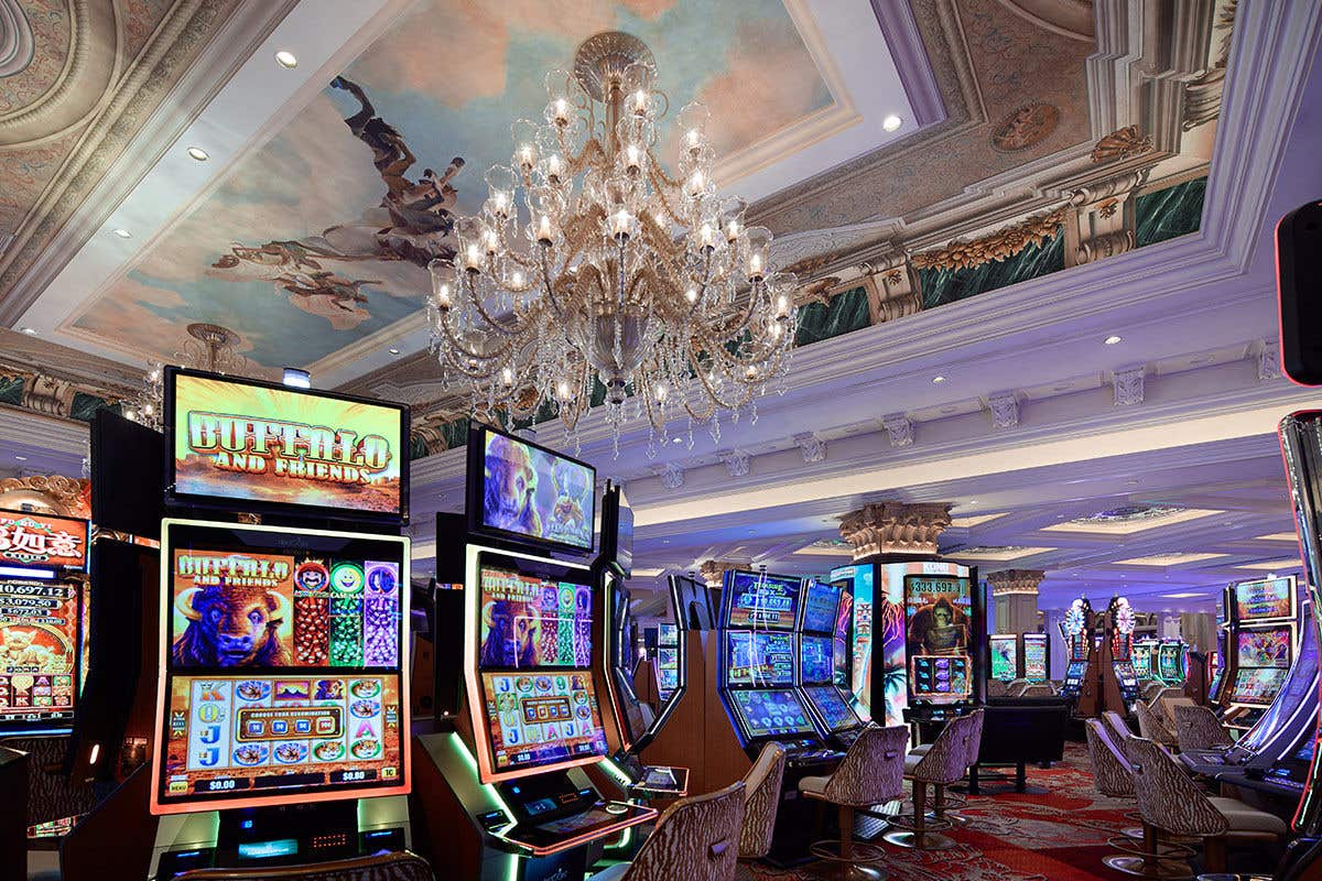 A lavish casino interior with rows of slot machines and a large chandelier.