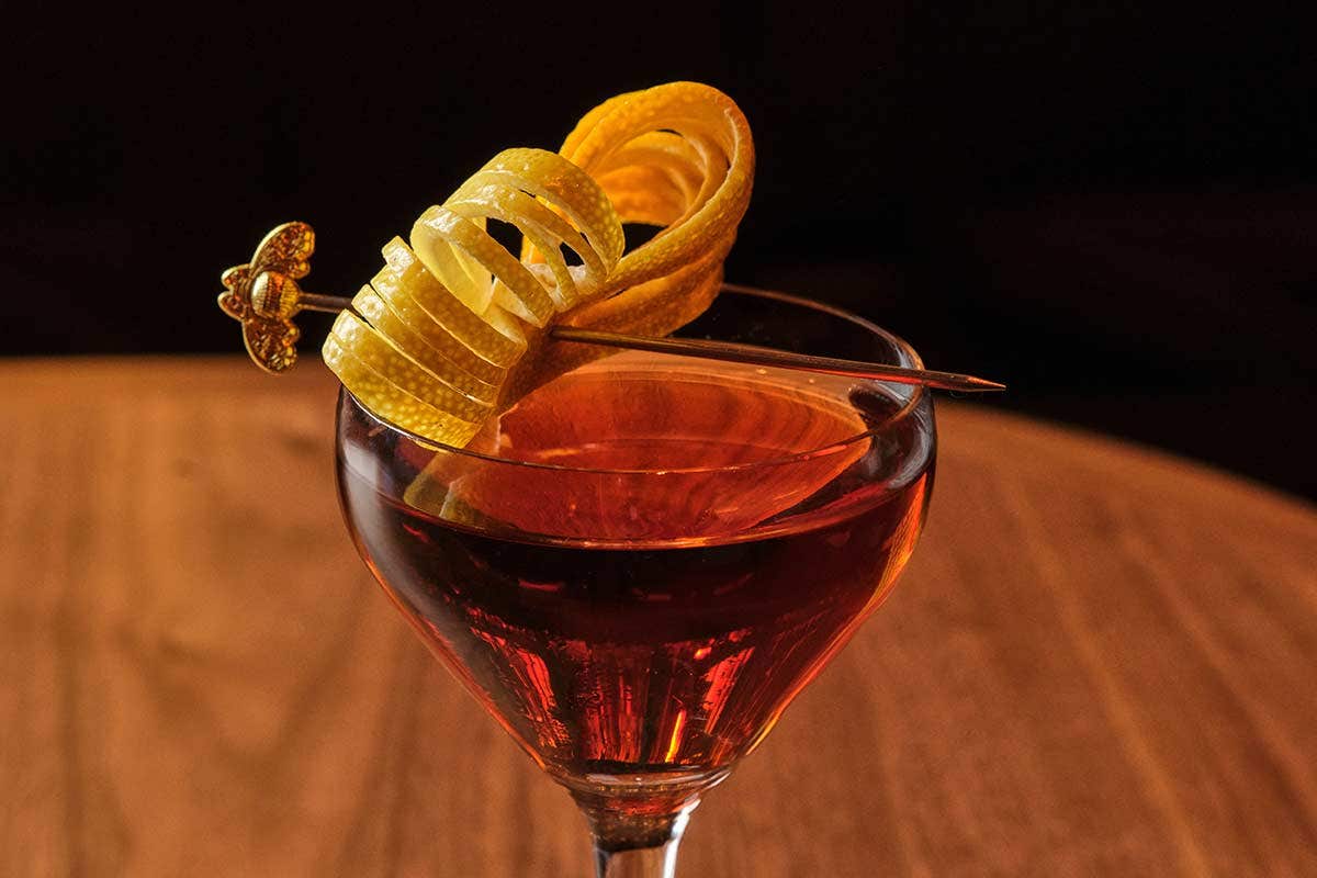 A cocktail garnished with a spiraled citrus peel and a decorative pick on a wooden table.