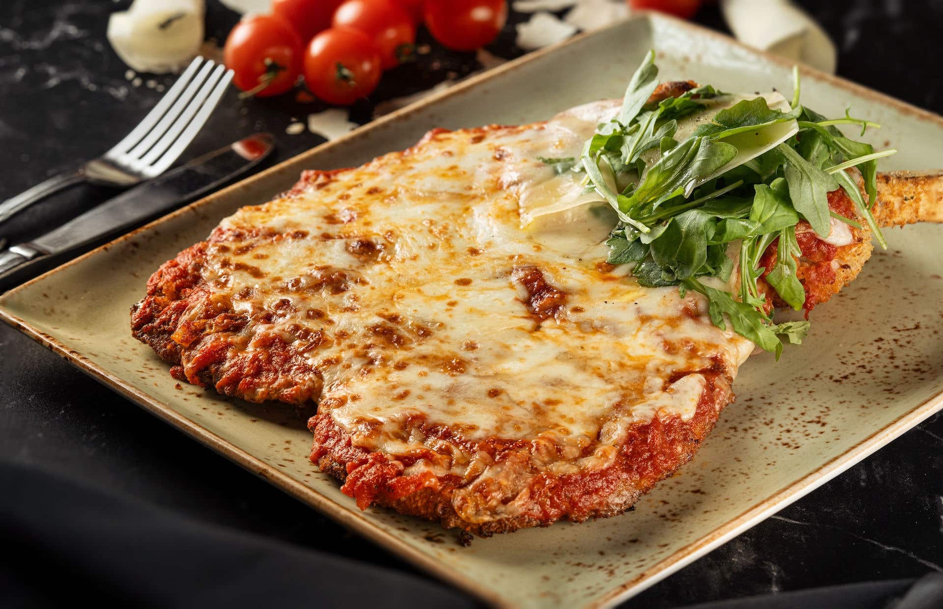 Veal parmigiana dish with melted cheese and herby garnish.