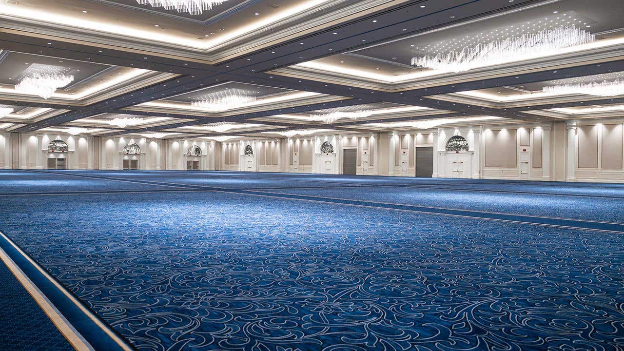 Large empty ballroom with white walls, blue carpet and chandeliers hanging from the ceiling.