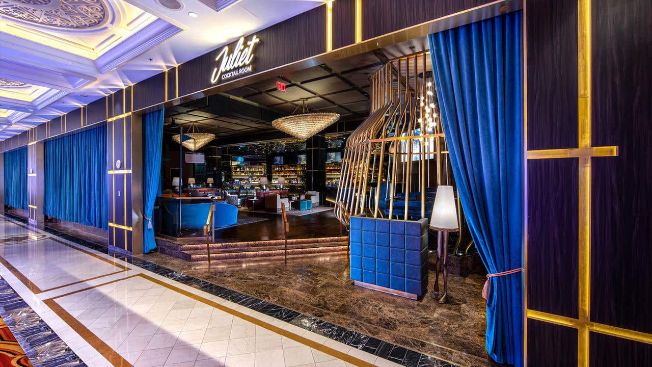 The entrance to Juliet Cocktail Room with signage and host stand visible and bright blue curtains.